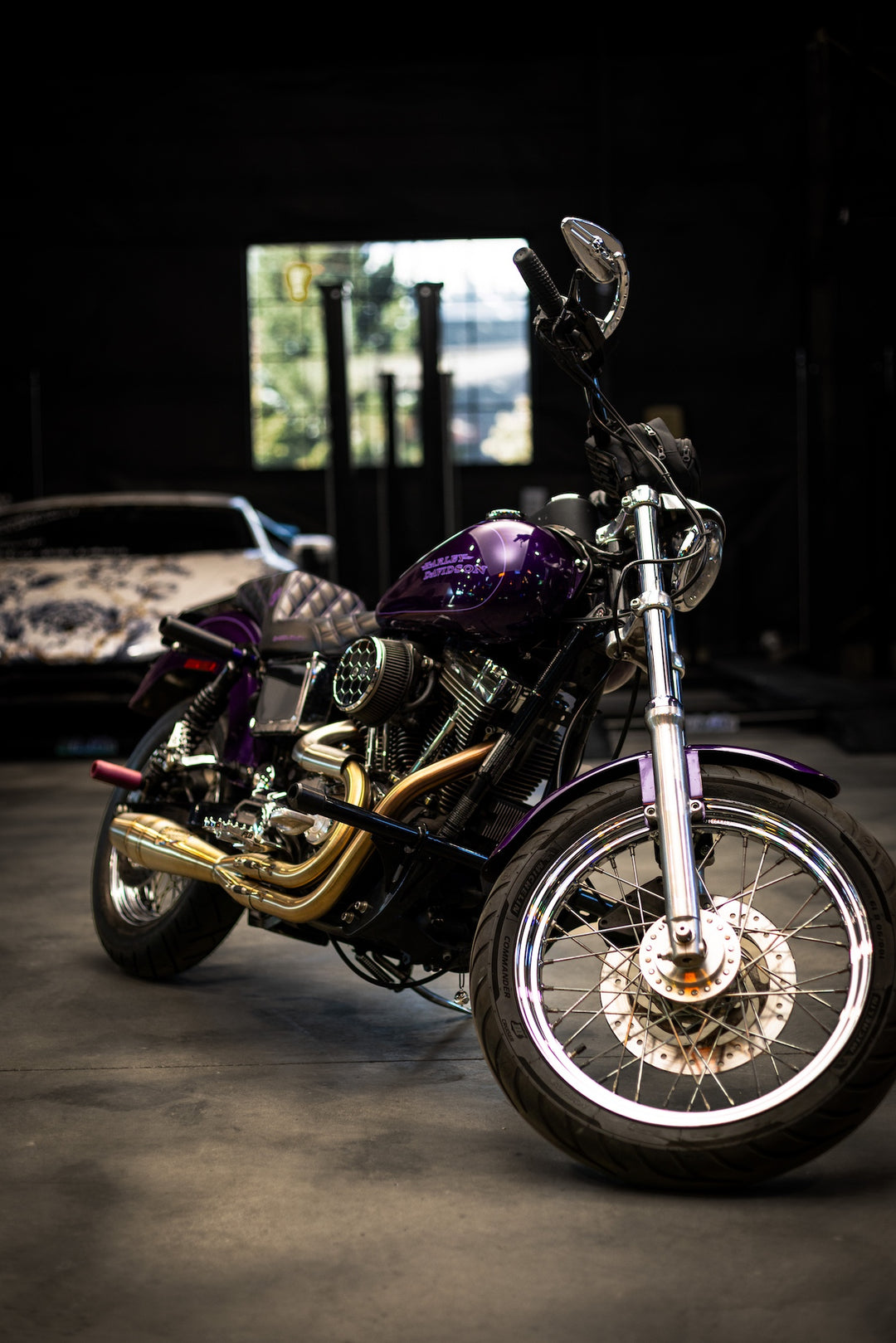 A purple Harley-Davidson Dyna motorcycle with Sawicki Speed 2-into-1 Shorty exhaust in brushed stainless steel finish, parked in a garage with a car int he background.