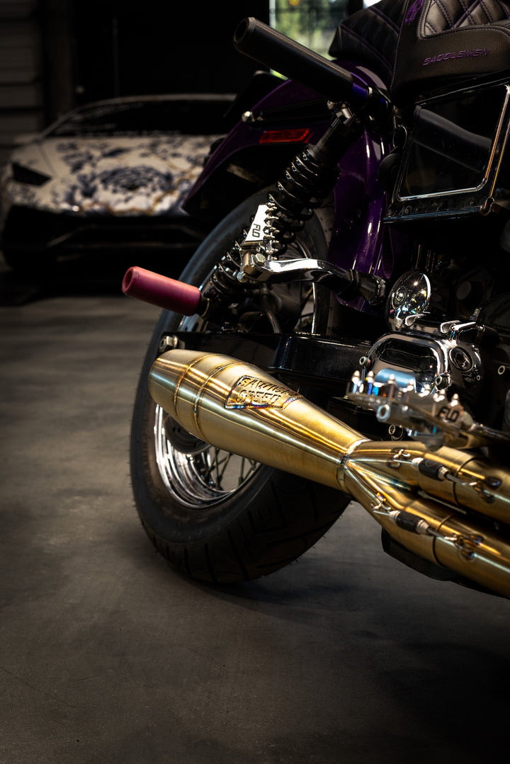 A closeup of a Sawicki Speed 2-into-1 Shorty exhaust in brushed stainless steel finish on a purple Harley-Davidson Dyna motorcycle.
